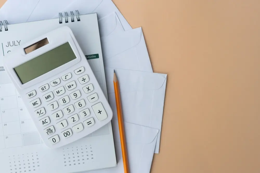 Calculator on a calendar with envelopes, representing the calculation of affordable monthly payments for a Canadian consumer proposal